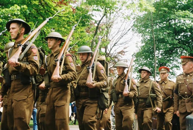 8 men dressed as British Tommys in 1945 uniform carry guns