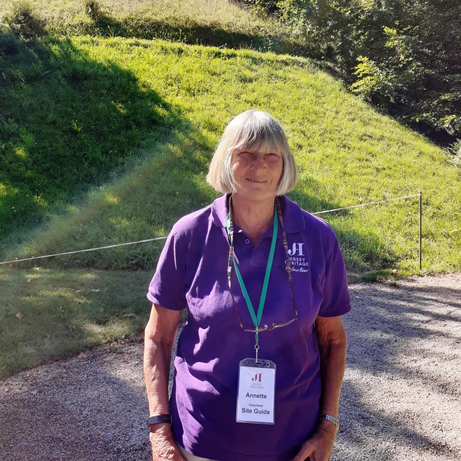 Jersey Heritage volunteer stands in front of La Hougue Bie