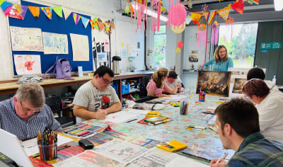 A small group of people sit at a table doing a colouring project