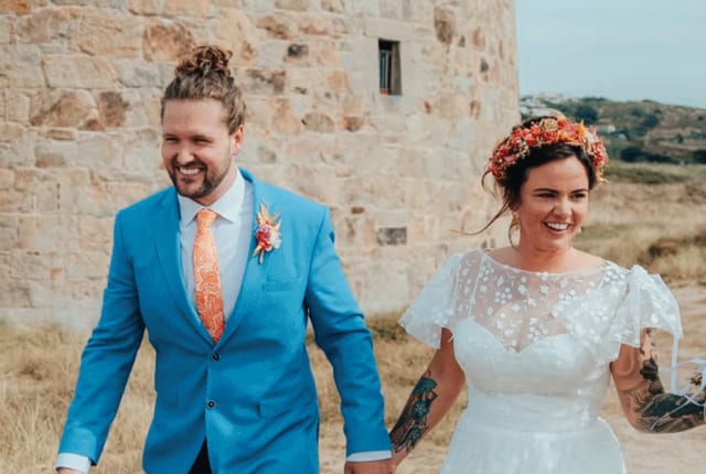 bride and groom walk away from an historic building in background