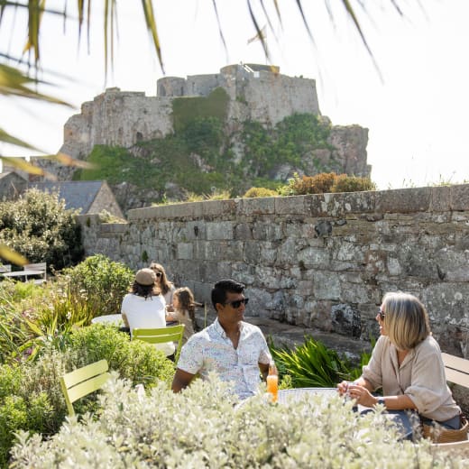 man and woman sit at an outside cafe with a castle in background