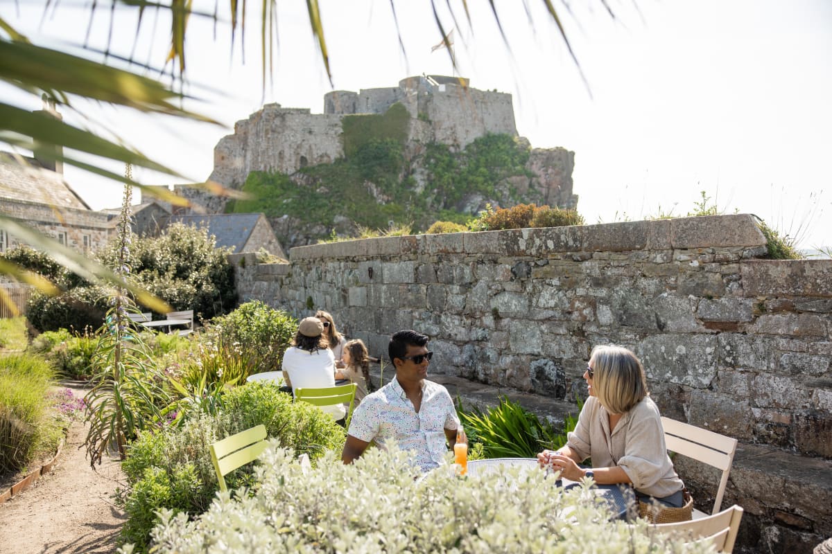 man and woman sit at an outside cafe with a castle in background